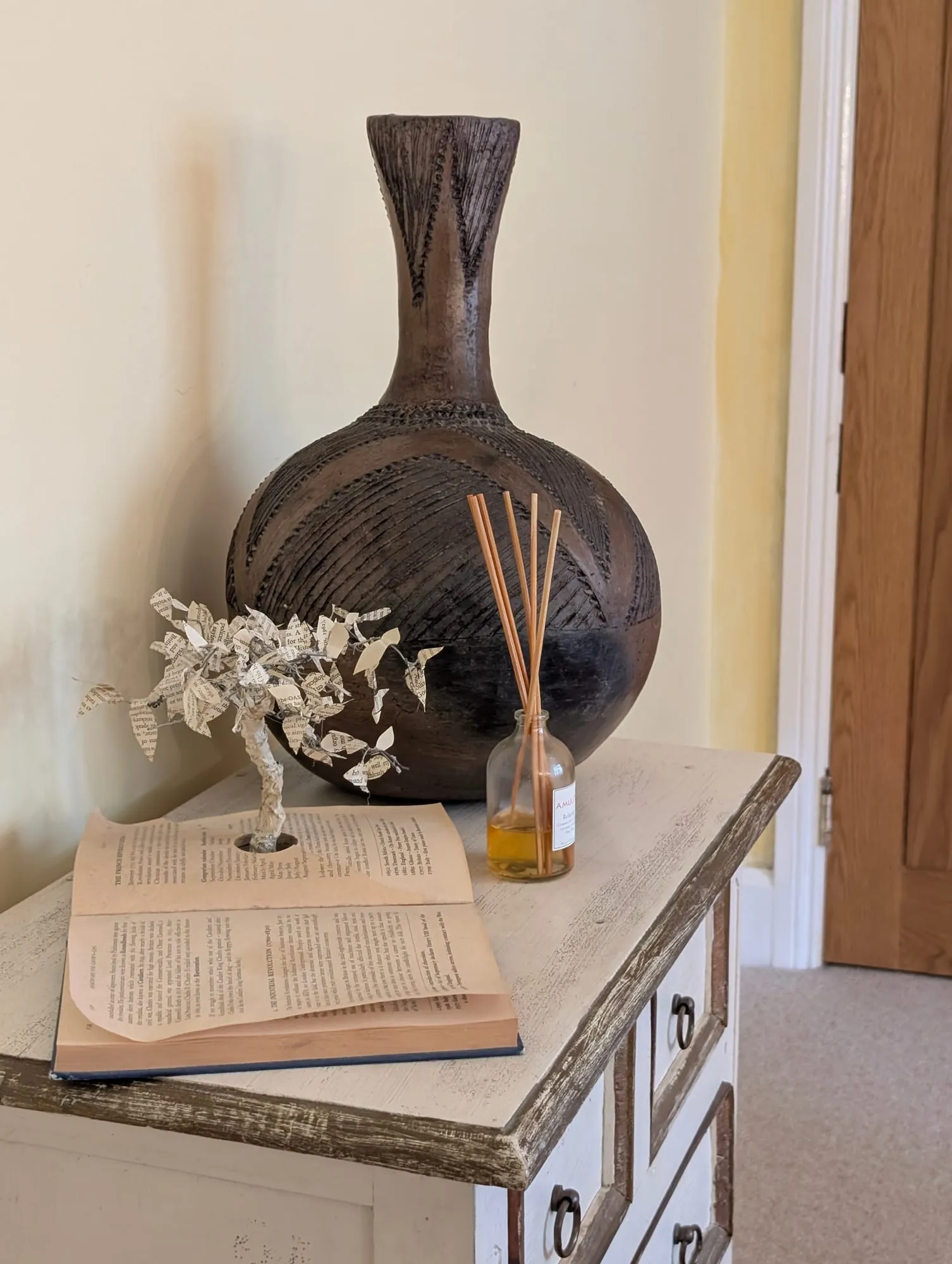 A book, paper tree, and dark vase on a painted cabinet in the consulting room